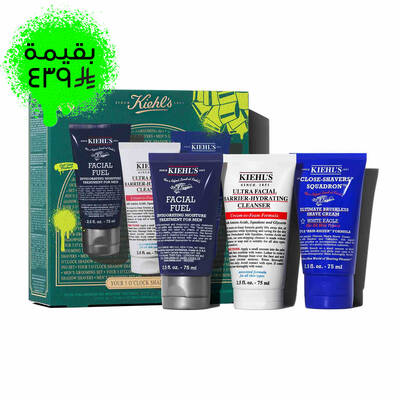 A graphic, set against a dark green textured background, features three Kiehl’s products. A white tube of "KIEHL’S ULTRA FACIAL BARRIER-HYDRATING CLEANSER" is labeled "TRAVEL SIZE" in bright green. A blue tube of "KIEHL’S 'CLOSE-SHAVERS' SQUADRON ULTIMATE BRUSHLESS SHAVE CREAM" is also labeled "TRAVEL SIZE" in bright green. A dark blue tube of "KIEHL’S FACIAL FUEL MOISTURIZER" is labeled "TRAVEL SIZE" in bright green. In the lower right, a partially visible green Kiehl’s gift box showcases the same three products.