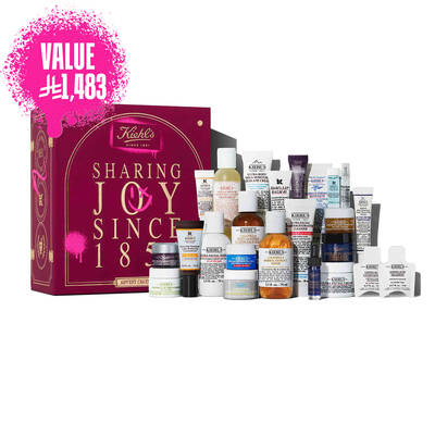 Kiehl’s Advent Calendar gift box in deep red with gold text, displayed next to 24 mini skincare products including Ultra Facial Cream, Calendula Toner, Retinol Serum, and Lip Balm #1. A pink spray-paint graphic on the side calls out the value of the set.