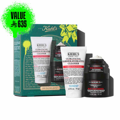 A graphic set against a dark green textured background with bright green accents features three Kiehl’s products and a gift box. On the left is a white tube of "KIEHL’S ULTRA FACIAL BARRIER-HYDRATING CLEANSER" labeled "TRAVEL SIZE." In the center are a black jar of "KIEHL’S AGE DEFENDER CREAM MOISTURIZER" and a black jar of "KIEHL’S AGE DEFENDER EYE REPAIR" with visible cream, both labeled "FULL SIZE." To the right is a boxed Kiehl’s gift set displaying the same three products, decorated with bright green graphic shapes and a bow design."