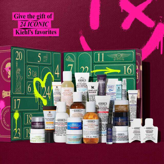 The Kiehl’s Advent Calendar is open, showcasing a festive green and gold drawer design with neon illustrations and the number 24highlighted in yellow. In front of the calendar, 24 mini Kiehl’s products are arranged in rows, including cleansers, toners, creams, serums, andhair care. A bright pink banner in the top left corner reads: “Give the gift of 24 ICONIC Kiehl’s favorites.” The background is deep burgundy withpink graffiti-style graphics.