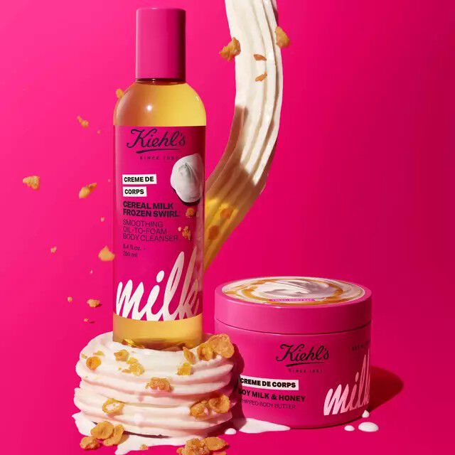 Two Kiehl's Creme de Corps products against a pink background: a Cereal Milk Frozen Swirl body cleanser bottle and a Soy Milk & Honey whipped body butter tub.​